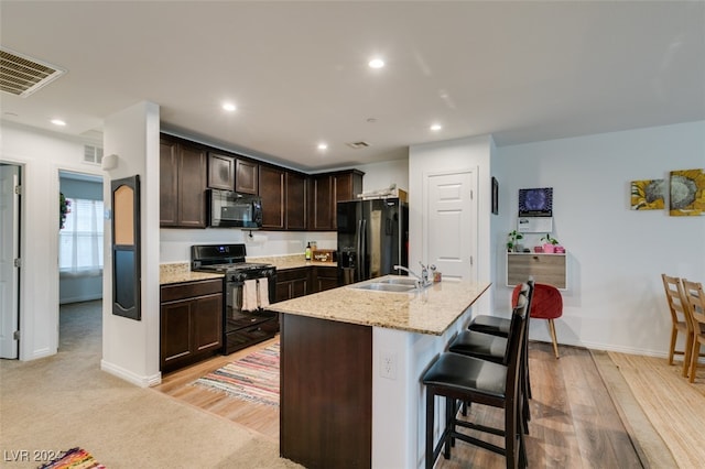 kitchen with light stone countertops, a kitchen island with sink, sink, black appliances, and a breakfast bar area