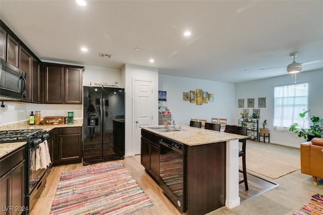 kitchen with sink, an island with sink, black appliances, and light wood-type flooring