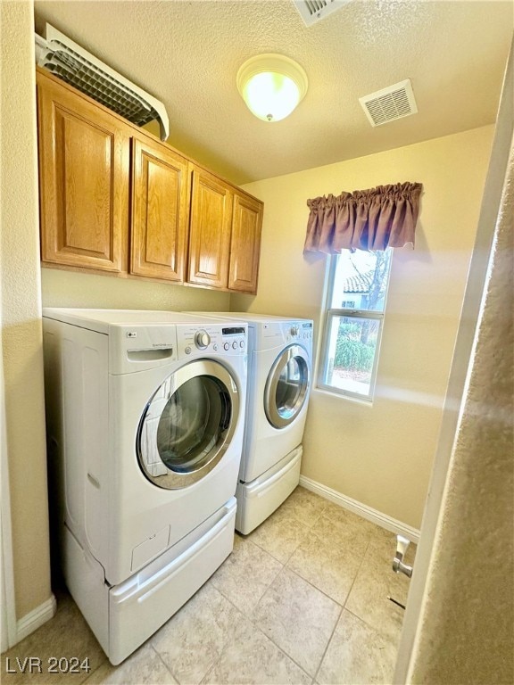 clothes washing area with cabinets, independent washer and dryer, a textured ceiling, and light tile patterned flooring