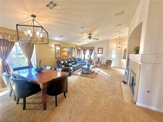 dining area with carpet flooring, ceiling fan with notable chandelier, a tile fireplace, and vaulted ceiling