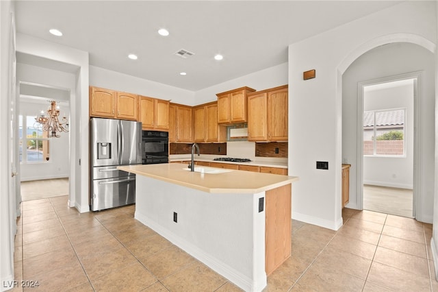 kitchen with decorative backsplash, stainless steel refrigerator with ice dispenser, sink, a center island with sink, and black oven