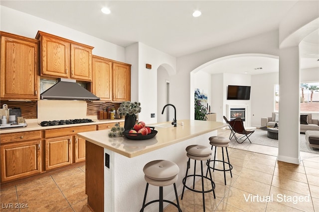 kitchen with sink, gas stovetop, decorative backsplash, a center island with sink, and light tile patterned floors