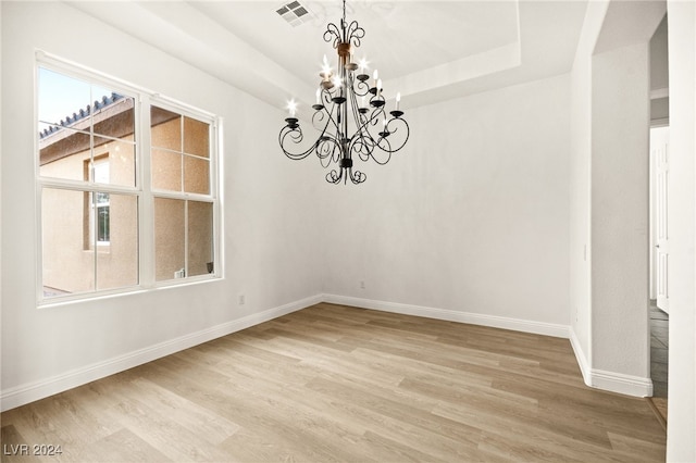 empty room with a raised ceiling, light wood-type flooring, and a notable chandelier