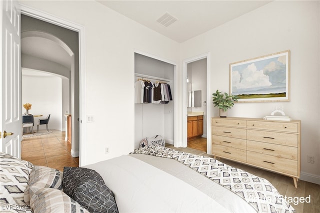 bedroom with ensuite bathroom, light hardwood / wood-style floors, and a closet