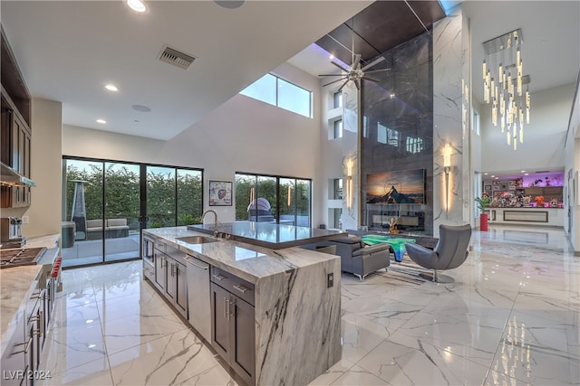 kitchen featuring light stone countertops, sink, stainless steel appliances, a towering ceiling, and a kitchen island with sink