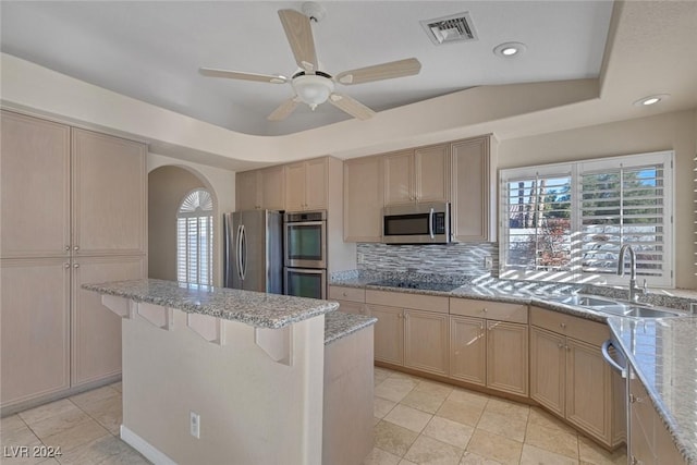 kitchen featuring sink, a tray ceiling, decorative backsplash, a breakfast bar, and appliances with stainless steel finishes