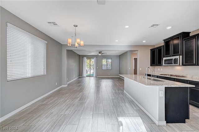 kitchen with appliances with stainless steel finishes, an island with sink, sink, hanging light fixtures, and light stone counters