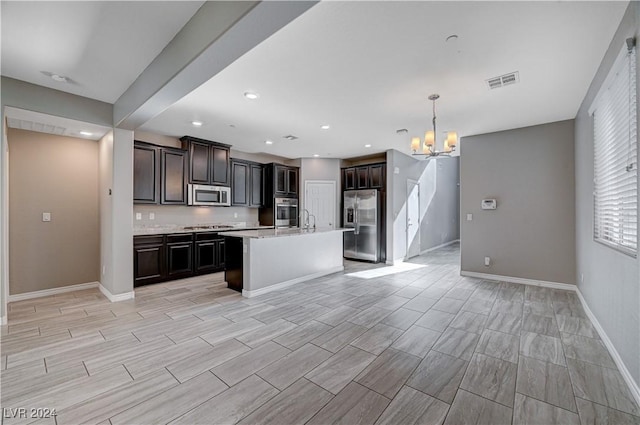 kitchen with sink, hanging light fixtures, a kitchen island with sink, stainless steel appliances, and an inviting chandelier