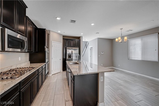 kitchen with pendant lighting, sink, a kitchen island with sink, stainless steel appliances, and light stone countertops