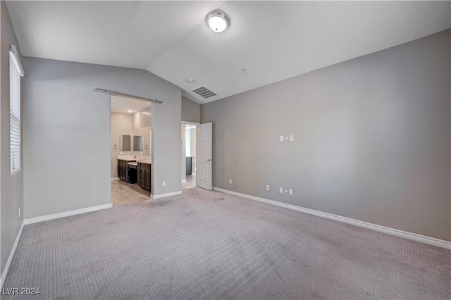 interior space with lofted ceiling, ensuite bathroom, a barn door, and light carpet