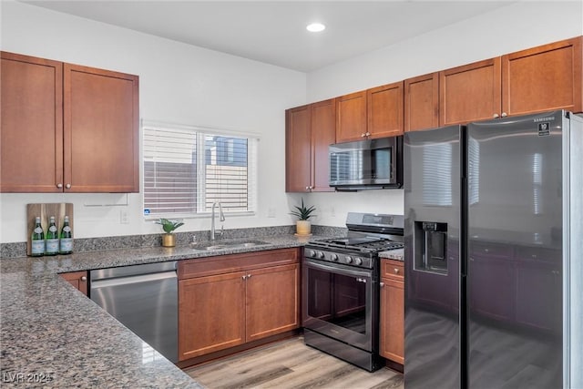 kitchen with sink, stainless steel appliances, light hardwood / wood-style floors, and dark stone counters