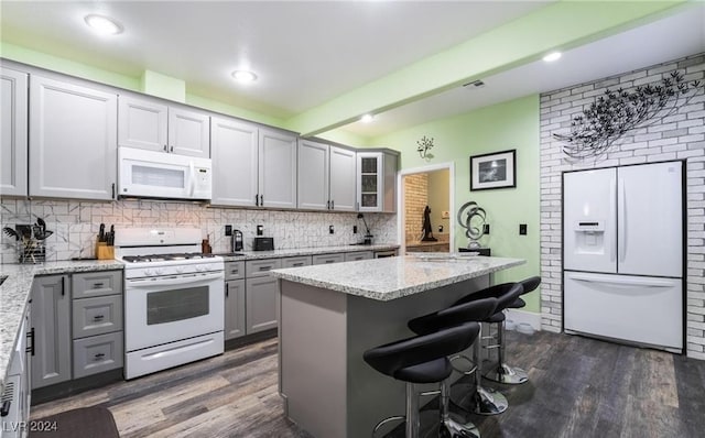 kitchen featuring light stone countertops, dark hardwood / wood-style floors, a kitchen breakfast bar, and white appliances