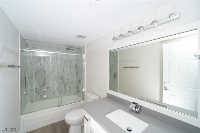 full bathroom with shower / bath combination with glass door, vanity, hardwood / wood-style flooring, and toilet