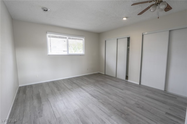 unfurnished bedroom featuring ceiling fan, light wood-type flooring, a textured ceiling, and two closets