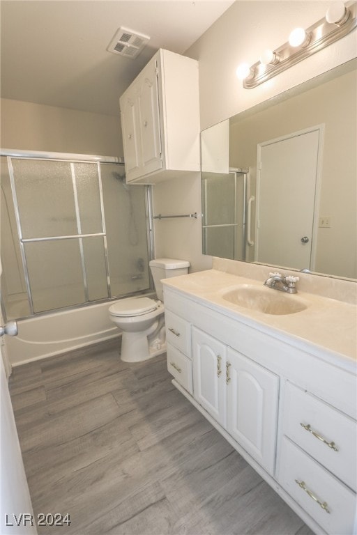 full bathroom featuring hardwood / wood-style floors, vanity, toilet, and enclosed tub / shower combo