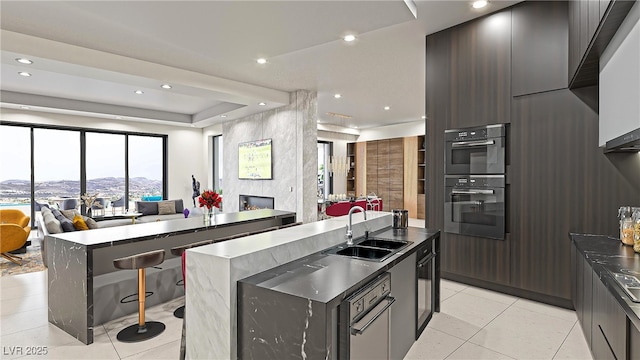 kitchen featuring a center island with sink, double wall oven, open floor plan, a sink, and modern cabinets