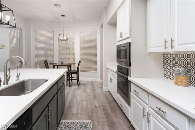 kitchen with sink, stainless steel appliances, pendant lighting, white cabinets, and light wood-type flooring