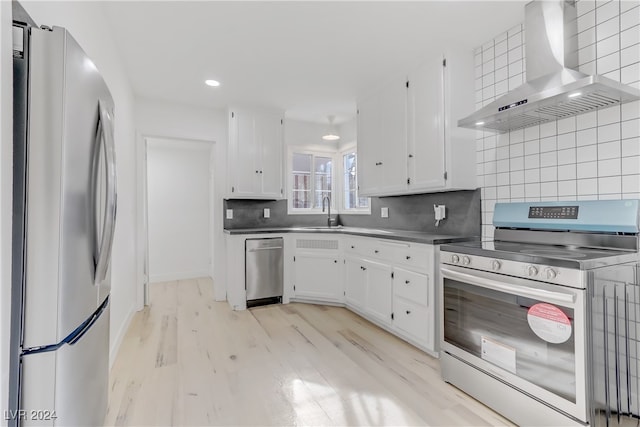 kitchen featuring backsplash, white cabinets, stainless steel appliances, and wall chimney range hood