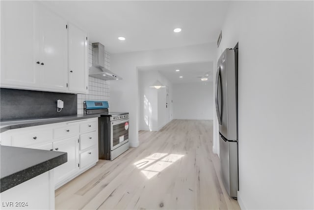 kitchen with appliances with stainless steel finishes, light hardwood / wood-style floors, white cabinetry, and wall chimney exhaust hood