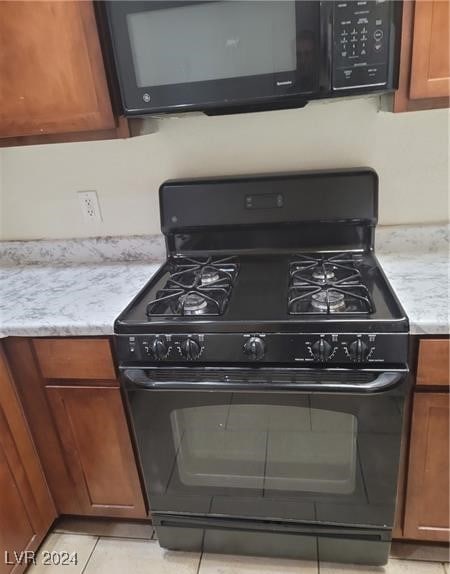 kitchen with black appliances, light tile patterned flooring, and light stone countertops