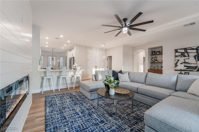 living room with built in shelves, ceiling fan, and light wood-type flooring