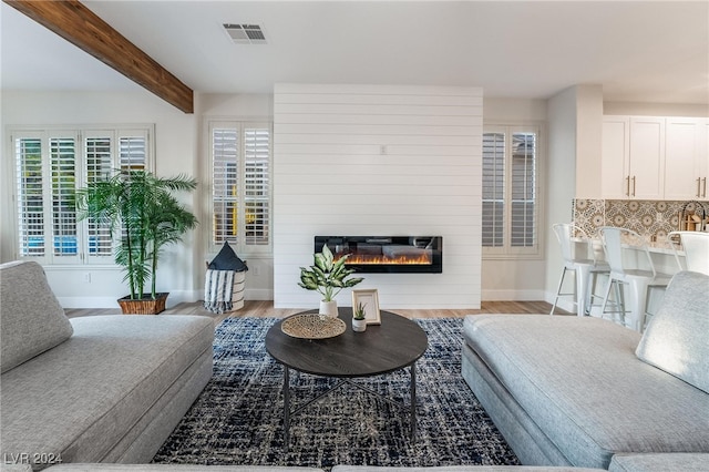 living room with beamed ceiling, light wood-type flooring, and a fireplace