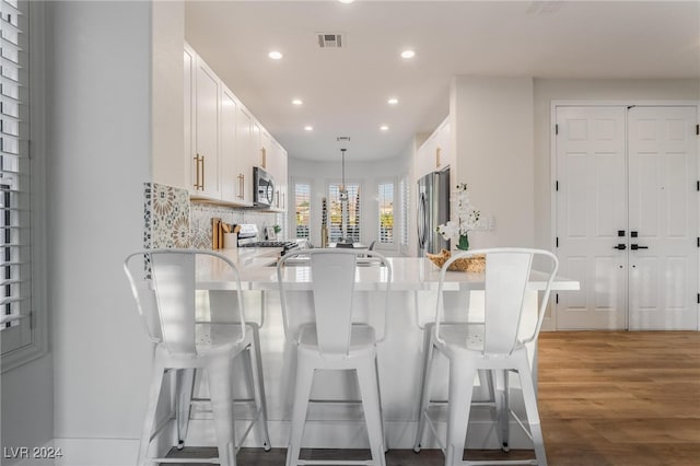 kitchen featuring kitchen peninsula, decorative backsplash, stainless steel appliances, wood-type flooring, and hanging light fixtures