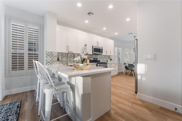 kitchen with a breakfast bar, backsplash, white cabinets, light wood-type flooring, and stainless steel appliances