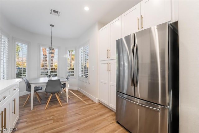 kitchen with white cabinetry, hanging light fixtures, stainless steel refrigerator, and light hardwood / wood-style flooring