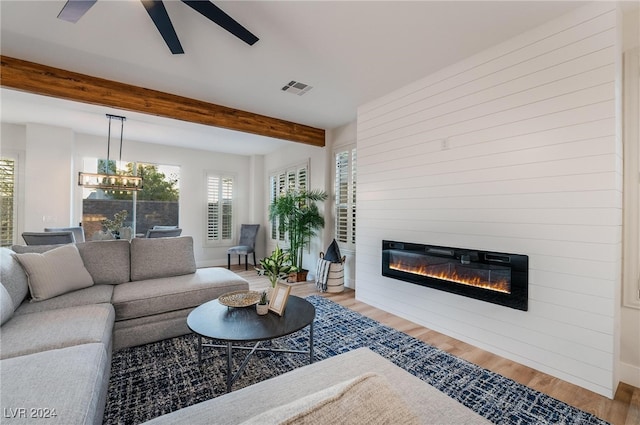 living room with ceiling fan with notable chandelier, a fireplace, beamed ceiling, and light wood-type flooring