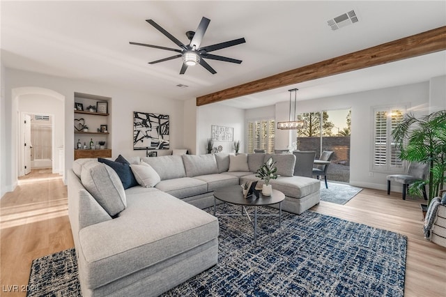 living room featuring beamed ceiling, ceiling fan, built in features, and light wood-type flooring