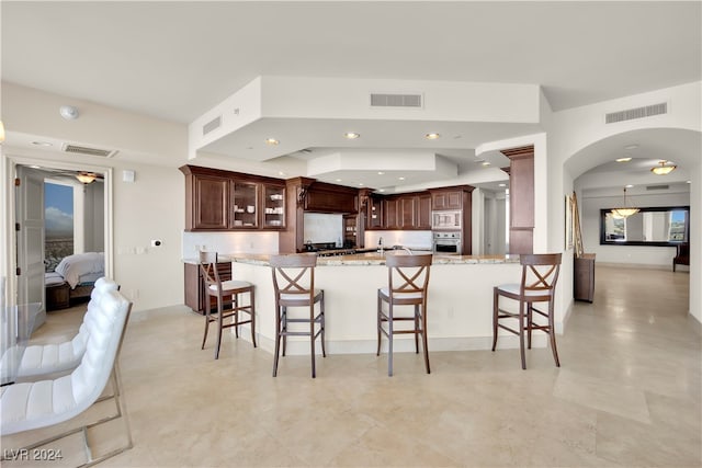 kitchen with dark brown cabinets, light stone countertops, a breakfast bar area, and appliances with stainless steel finishes