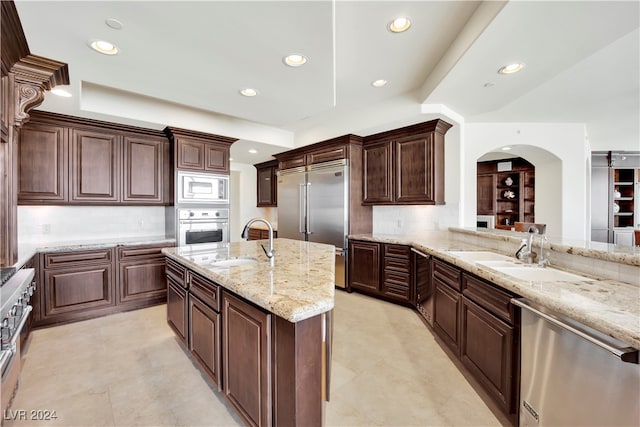 kitchen with built in appliances, backsplash, light stone counters, and sink