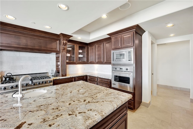 kitchen featuring sink, light stone counters, backsplash, dark brown cabinets, and appliances with stainless steel finishes