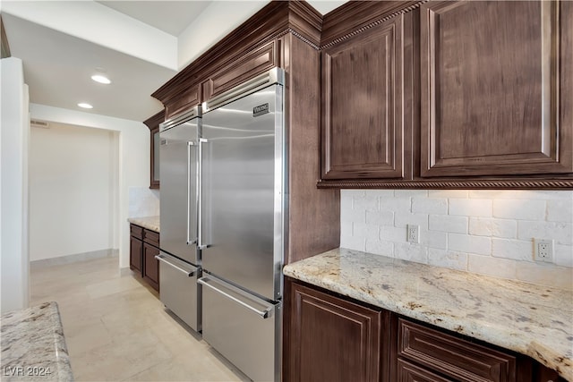 kitchen featuring backsplash, light stone counters, dark brown cabinets, and stainless steel built in refrigerator