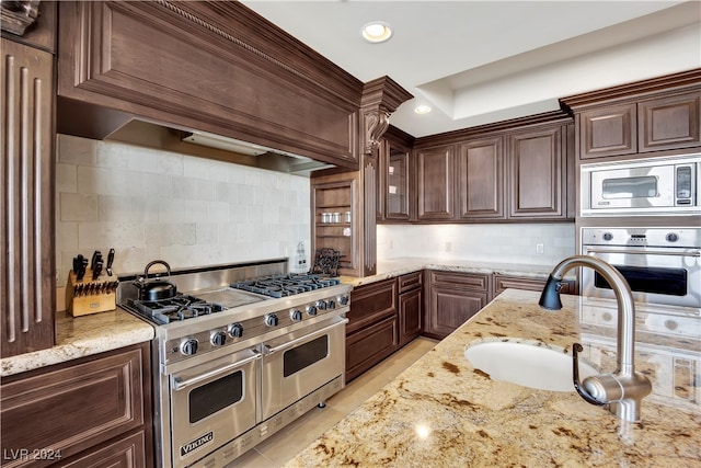 kitchen with tasteful backsplash, dark brown cabinets, stainless steel appliances, and premium range hood