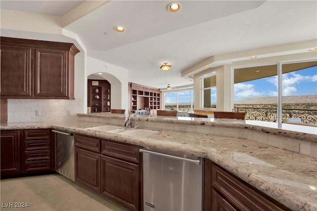 kitchen with light stone countertops, decorative backsplash, stainless steel dishwasher, and sink