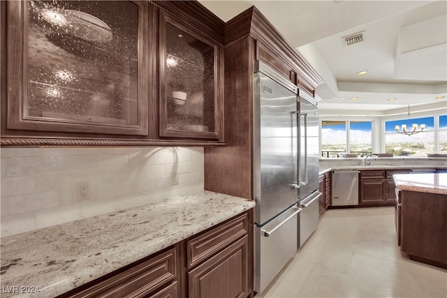 kitchen featuring pendant lighting, dark brown cabinets, light stone counters, stainless steel appliances, and a chandelier