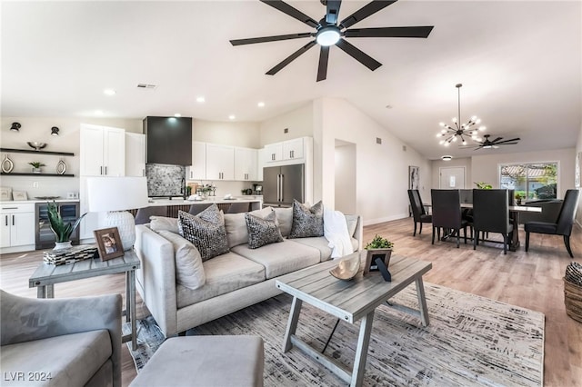 living room featuring ceiling fan with notable chandelier, beverage cooler, lofted ceiling, and light wood-type flooring