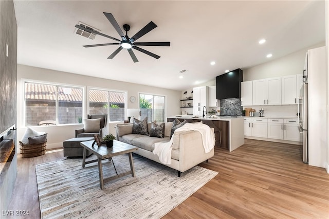 living room with ceiling fan, light wood-type flooring, sink, and vaulted ceiling