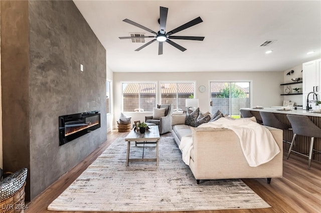 living room featuring ceiling fan, a large fireplace, and hardwood / wood-style flooring