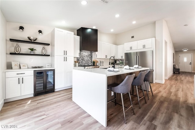 kitchen with wine cooler, white cabinetry, a center island with sink, and light hardwood / wood-style flooring