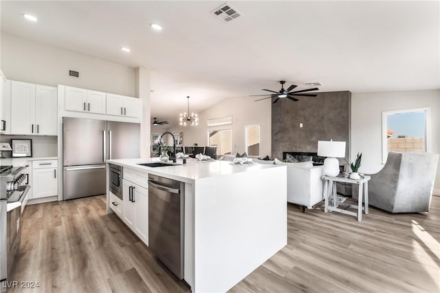 kitchen featuring hanging light fixtures, built in appliances, vaulted ceiling, a kitchen island with sink, and white cabinets