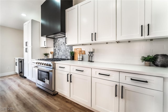 kitchen featuring light wood-type flooring, tasteful backsplash, wall chimney exhaust hood, stainless steel stove, and white cabinetry