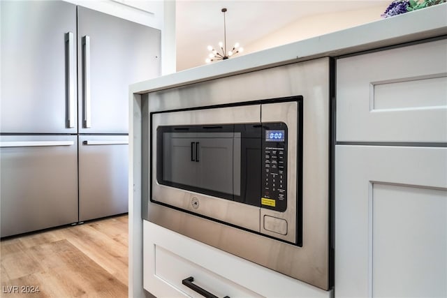 room details with pendant lighting, white cabinets, light wood-type flooring, a notable chandelier, and stainless steel appliances