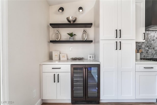 bar with backsplash, white cabinets, beverage cooler, and wall chimney range hood