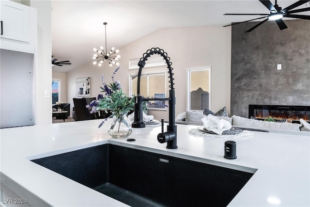 kitchen featuring white cabinets, vaulted ceiling, sink, an inviting chandelier, and a fireplace