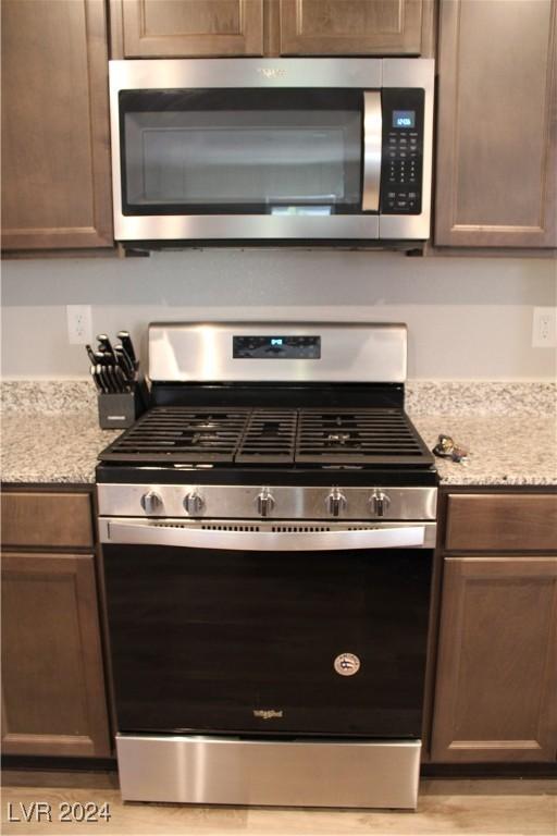 kitchen with appliances with stainless steel finishes, dark brown cabinetry, light wood-style flooring, and light stone counters