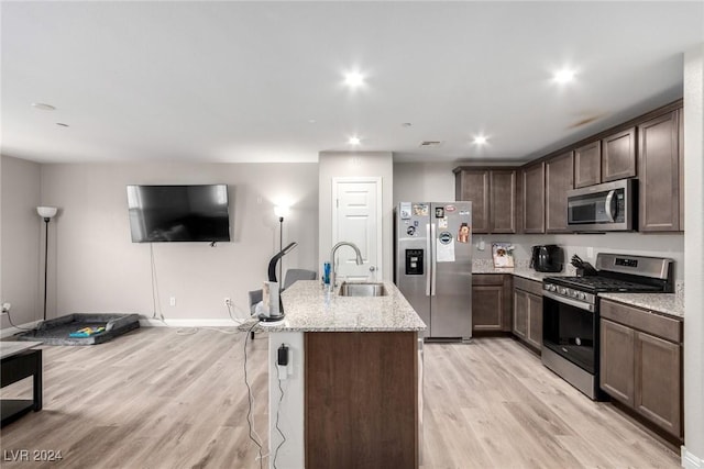 kitchen featuring light stone counters, light wood-style flooring, a sink, dark brown cabinets, and appliances with stainless steel finishes