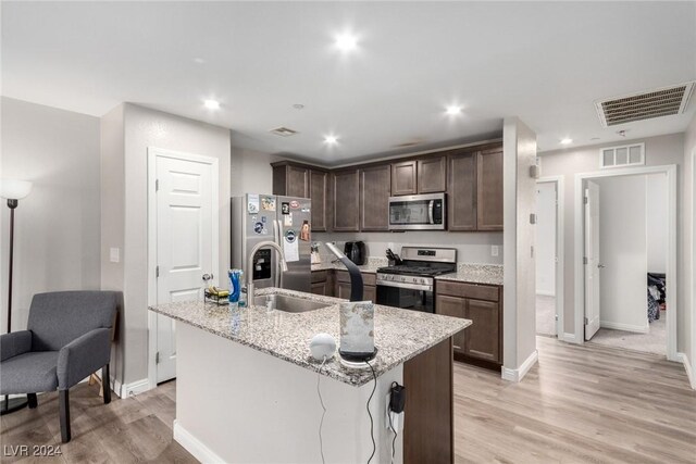 kitchen featuring light stone counters, dark brown cabinetry, visible vents, appliances with stainless steel finishes, and a center island with sink